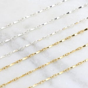May include: Four silver and gold chains on a white marble surface. The chains are all the same style, but different lengths. The chains are made of small, flat links.