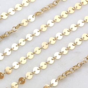 May include: Four gold chains with round, flat, linked discs. The chains are arranged in a staggered pattern on a white surface.