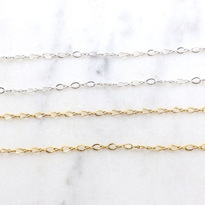 May include: Four chains of different lengths, two silver and two gold, are laid out on a white marble surface. The chains are all made of small, oval-shaped links.
