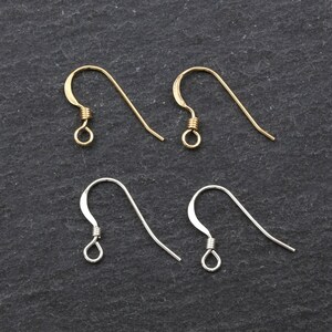 May include: Four earring hooks, two gold and two silver, on a black background.