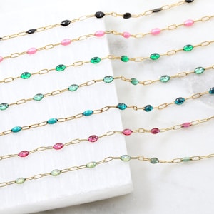May include: A set of eight gold chains with different colored beads. The beads are oval shaped and have a glossy finish. The chains are arranged in a staggered pattern, with the top chain being the shortest and the bottom chain being the longest.