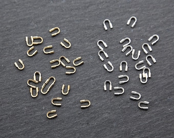 May include: A close-up of two groups of small metal loops. One group is silver and the other is gold. The loops are arranged in a random pattern on a dark gray surface.