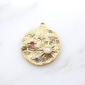 May include: Gold-colored pendant with a textured surface, featuring a sunburst design with an opal center and surrounding star accents. The pendant also includes a red and blue gemstone, and several clear crystals.