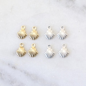 May include: Six small seashell charms, three gold and three silver, on a white marble surface.
