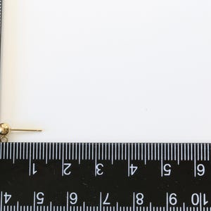 May include: A gold-toned earring finding with a small ball at the top and a straight post. The finding is measured against a ruler.