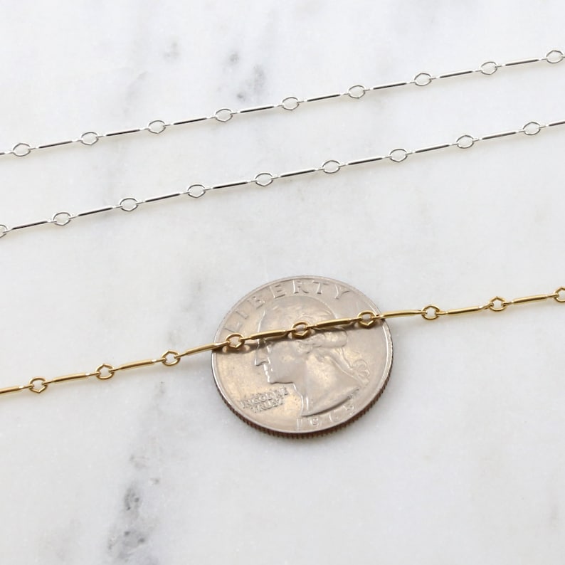 Puede incluir: Dos cadenas, una plateada y otra dorada, se colocan sobre una superficie de m&aacute;rmol blanco. Una moneda de 25 centavos de d&oacute;lar estadounidense se coloca entre las cadenas para mostrar la escala.