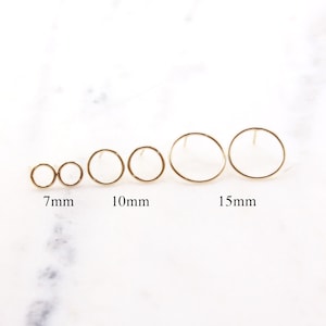 May include: Five pairs of gold hoop earrings in different sizes: 7mm, 10mm, and 15mm. The earrings are displayed on a white marble surface.