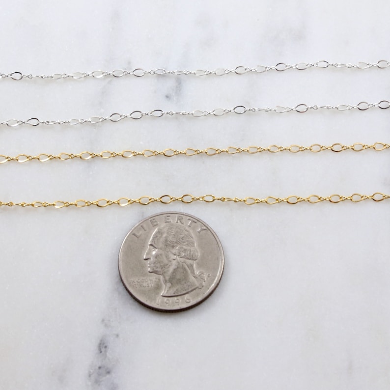 May include: Three gold and silver chains laid out on a white marble surface. A US quarter is placed below the chains for size comparison.