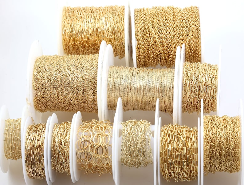 Peut inclure: Plusieurs rouleaux de cha&icirc;nes dor&eacute;es, chacun avec un design de maillon unique. Les bobines sont dispos&eacute;es sur une surface blanche, pr&eacute;sentant divers styles de cha&icirc;nes, notamment des motifs de perles, ovales et &agrave; maillons carr&eacute;s. Les cha&icirc;nes sont enroul&eacute;es sur des bobines blanches.