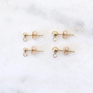 May include: Four gold-toned earring findings with a small loop at the bottom and a post on the back.