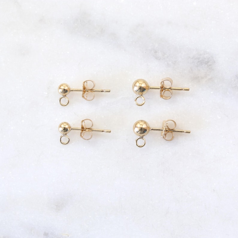 May include: Four gold-toned earring findings with a small loop at the bottom and a post on the back.