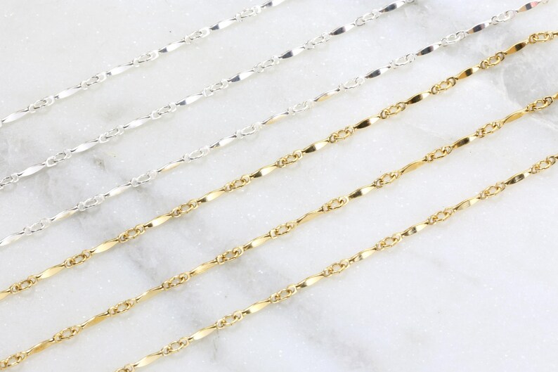 May include: Four silver and gold chains on a white marble surface. The chains are all the same style, but different lengths. The chains are made of small, flat links.