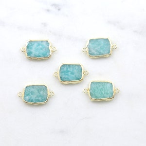 May include: Five gold-rimmed, rectangular, teal green gemstone connectors. The connectors have a rough, natural edge and are perfect for jewelry making.