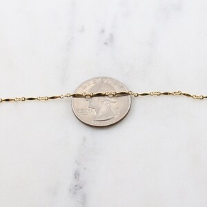 May include: A gold chain necklace with a delicate, flat, oval-shaped link. The chain is laid out on a white surface next to a US quarter for size comparison.