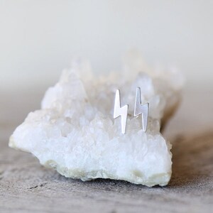 May include: A pair of silver lightning bolt stud earrings on a white crystal rock.