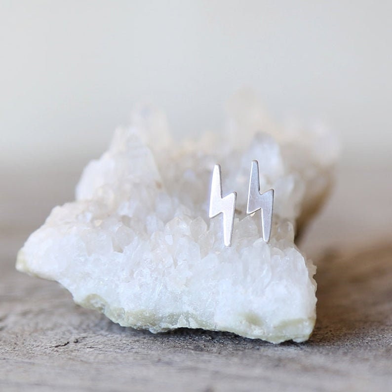 May include: A pair of silver lightning bolt stud earrings on a white crystal rock.