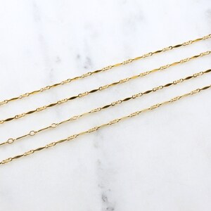 May include: Four gold chains with a delicate, flat, oval link design. The chains are layered on a white marble surface.