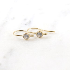 Puede incluir: Un par de pendientes de color dorado con un pequeño cristal transparente en cada pendiente.