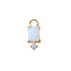 Peut inclure: Breloque en or avec une pierre d'opale blanche et un petit strass transparent. Le breloque a une boucle en haut pour l'attacher à un collier ou un bracelet.