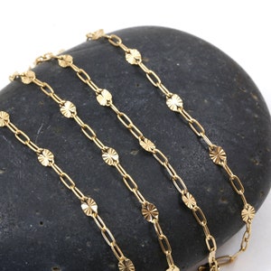 May include: Gold chain necklace with small, round, textured charms. The chain is shown in multiple layers on a dark gray stone.
