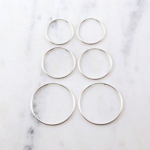May include: Set of five silver hoop earrings in different sizes. The earrings are arranged in a row from smallest to largest.