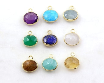 May include: Nine gemstone pendants in various colors, including purple, turquoise, and green, are displayed. Each pendant has a gold-colored bezel and a small loop for attaching to a chain or other jewelry. The pendants are arranged on a white surface.