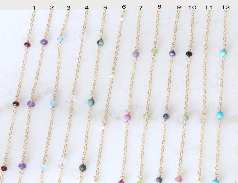 Peut inclure: Une collection de colliers d&eacute;licats en cha&icirc;ne dor&eacute;e, chacun orn&eacute; d'une seule pierre pr&eacute;cieuse. Les pierres pr&eacute;cieuses varient en couleur, notamment rouge, violet, bleu, vert et turquoise. Les colliers sont pr&eacute;sent&eacute;s sur une surface blanche.