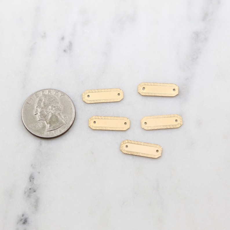 May include: Five gold-colored metal rectangular tags with two holes each. The tags have a textured design around the edges.