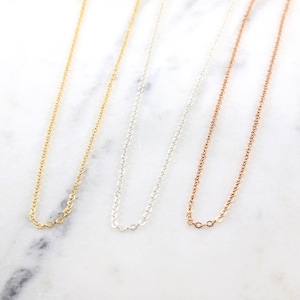 May include: Three delicate chain necklaces in gold, silver, and rose gold. The chains are all the same length and style, with a simple, classic design.