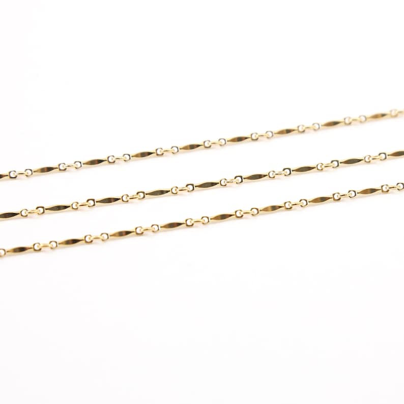 May include: Three gold chains with a flat, rectangular link design. The chains are laid out in parallel lines on a white background.