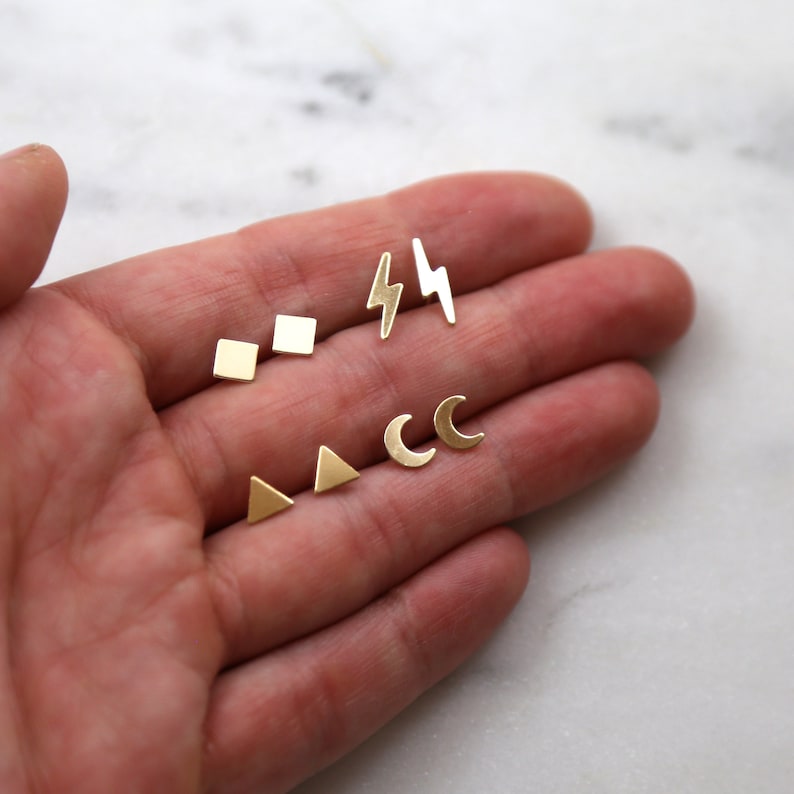 May include: A set of five gold earrings with different geometric shapes: a square, a triangle, a crescent moon, and two lightning bolts.
