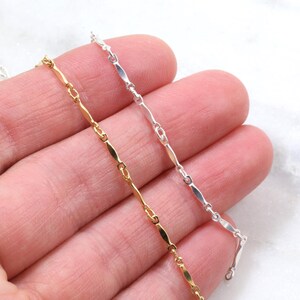 May include: Three chains of different colors: gold, silver, and white. The chains are made of small, flat, oval-shaped links.