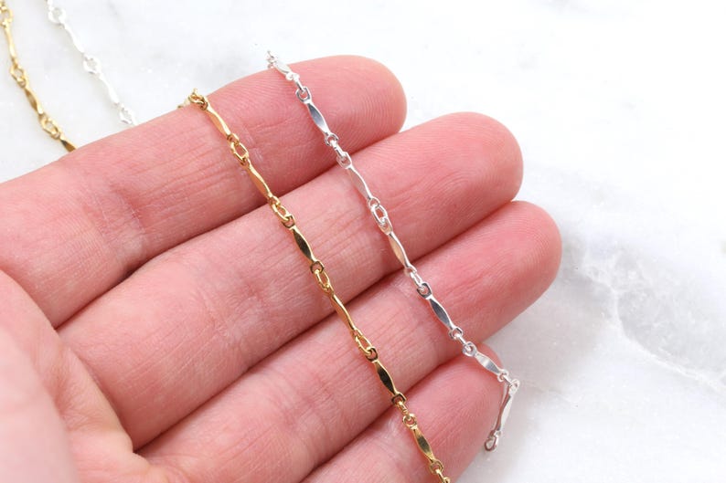 May include: Three chains of different colors: gold, silver, and white. The chains are made of small, flat, oval-shaped links.