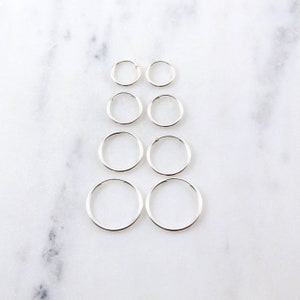 May include: Set of six silver hoop earrings of varying sizes. The earrings are arranged in three rows of two, with the smallest earrings at the top and the largest earrings at the bottom.