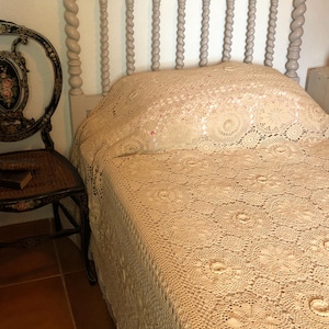 Peut inclure: Un lit blanc avec une couverture en crochet et une tête de lit en bois torsadée. La couverture a un motif floral délicat.