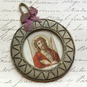 May include: A round, fabric-covered frame with a silver trim and a small image of Jesus Christ inside. The frame is decorated with a purple ribbon.