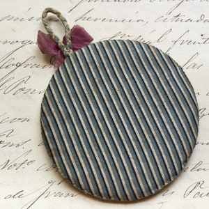 May include: A round, blue and white striped fabric ornament with a pink ribbon attached to the top.