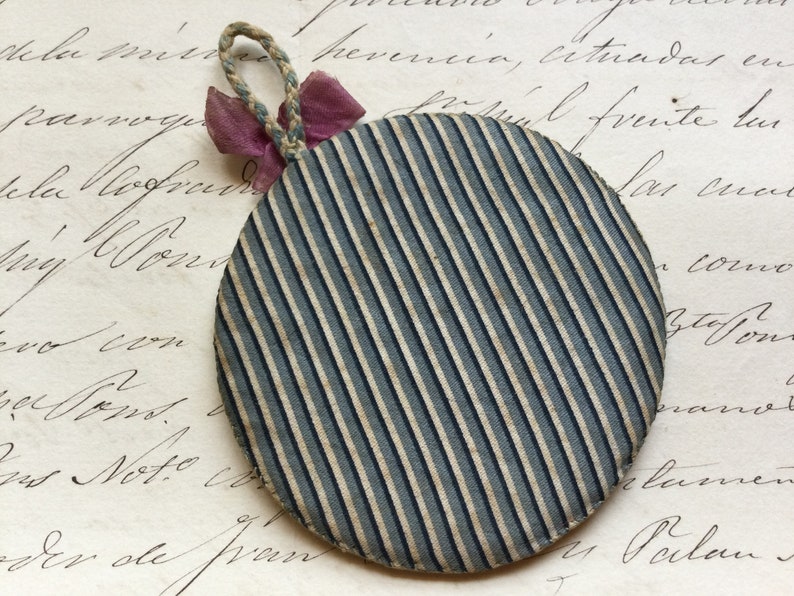 May include: A round, blue and white striped fabric ornament with a pink ribbon attached to the top.