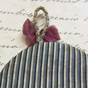 May include: A round, blue and white striped fabric ornament with a pink ribbon and a braided rope loop.