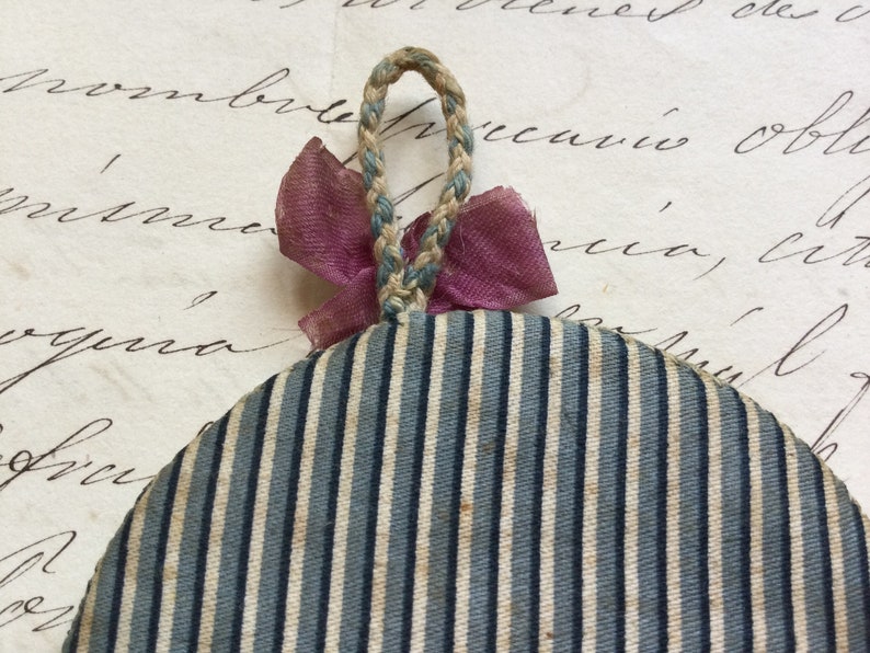 May include: A round, blue and white striped fabric ornament with a pink ribbon and a braided rope loop.