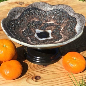 May include: A black and white ceramic fruit bowl with a raised, textured design. The bowl has a black pedestal base.