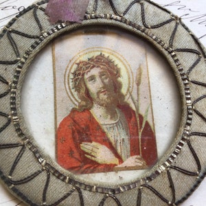 May include: A vintage, oval-shaped, fabric-covered frame with a woven design in black and silver. The frame contains a printed image of Jesus Christ wearing a crown of thorns and a red robe.