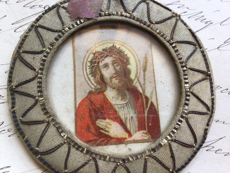 May include: A vintage, oval-shaped, fabric-covered frame with a woven design in black and silver. The frame contains a printed image of Jesus Christ wearing a crown of thorns and a red robe.