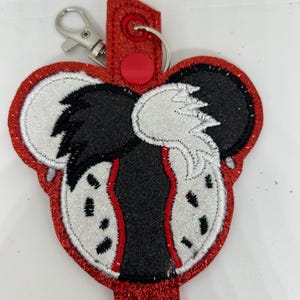 Könnte beinhalten: Ein roter, glitzernder Schlüsselanhänger mit einem schwarz-weißen Design. Das Design hat einen roten Rand und einen silbernen Verschluss. Der Schlüsselanhänger hat einen roten Riemen mit einem roten Knopf.