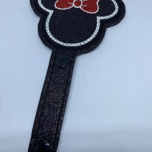 Könnte beinhalten: Schwarzer Glitzer-Schlüsselanhänger mit einer roten Glitzer-Schleife und einer weißen Umrandung in Form von Mickeys Kopf.