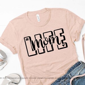 May include: A light pink t-shirt with a black graphic that says "#momlife" with a small heart in the "e".