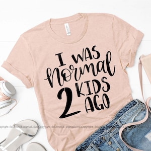 May include: A light pink t-shirt with black text that reads "I was normal 2 kids ago".