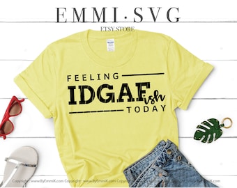May include: A yellow t-shirt with black text that reads "Feeling IDGAFish Today". The shirt is on a white wooden surface with a pair of sunglasses and a pair of sandals. The text is in a bold, blocky font.