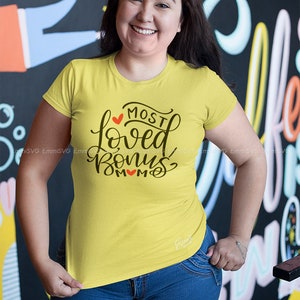 Pode incluir: Uma camiseta amarela com um gr&aacute;fico preto que diz "Most Loved Bonus Mom" com um cora&ccedil;&atilde;o vermelho no gr&aacute;fico.