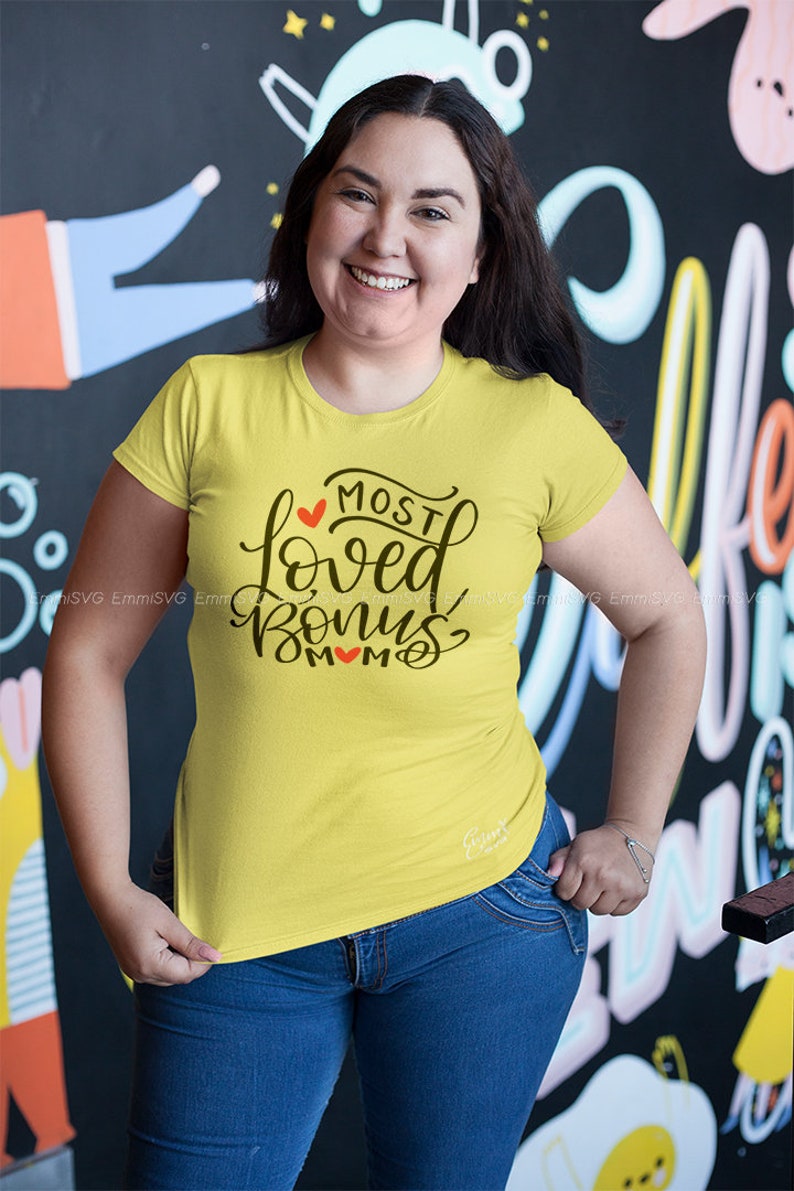 Pode incluir: Uma camiseta amarela com um gr&aacute;fico preto que diz "Most Loved Bonus Mom" com um cora&ccedil;&atilde;o vermelho no gr&aacute;fico.